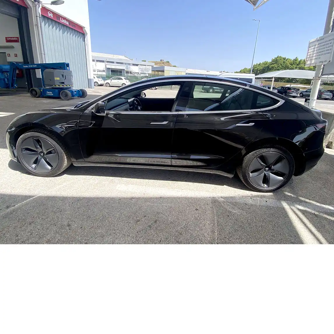 Tesla Model 3 Long Range preto visto de perfil lateral esquerdo, estacionado em zona industrial com iluminação solar