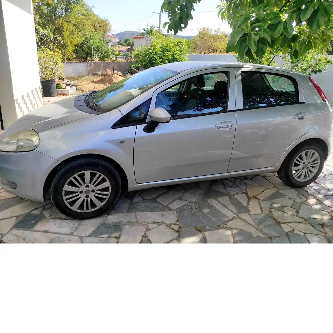 Fiat Punto prateado de 5 portas visto de perfil lateral esquerdo, estacionado em pátio exterior com piso em pedra