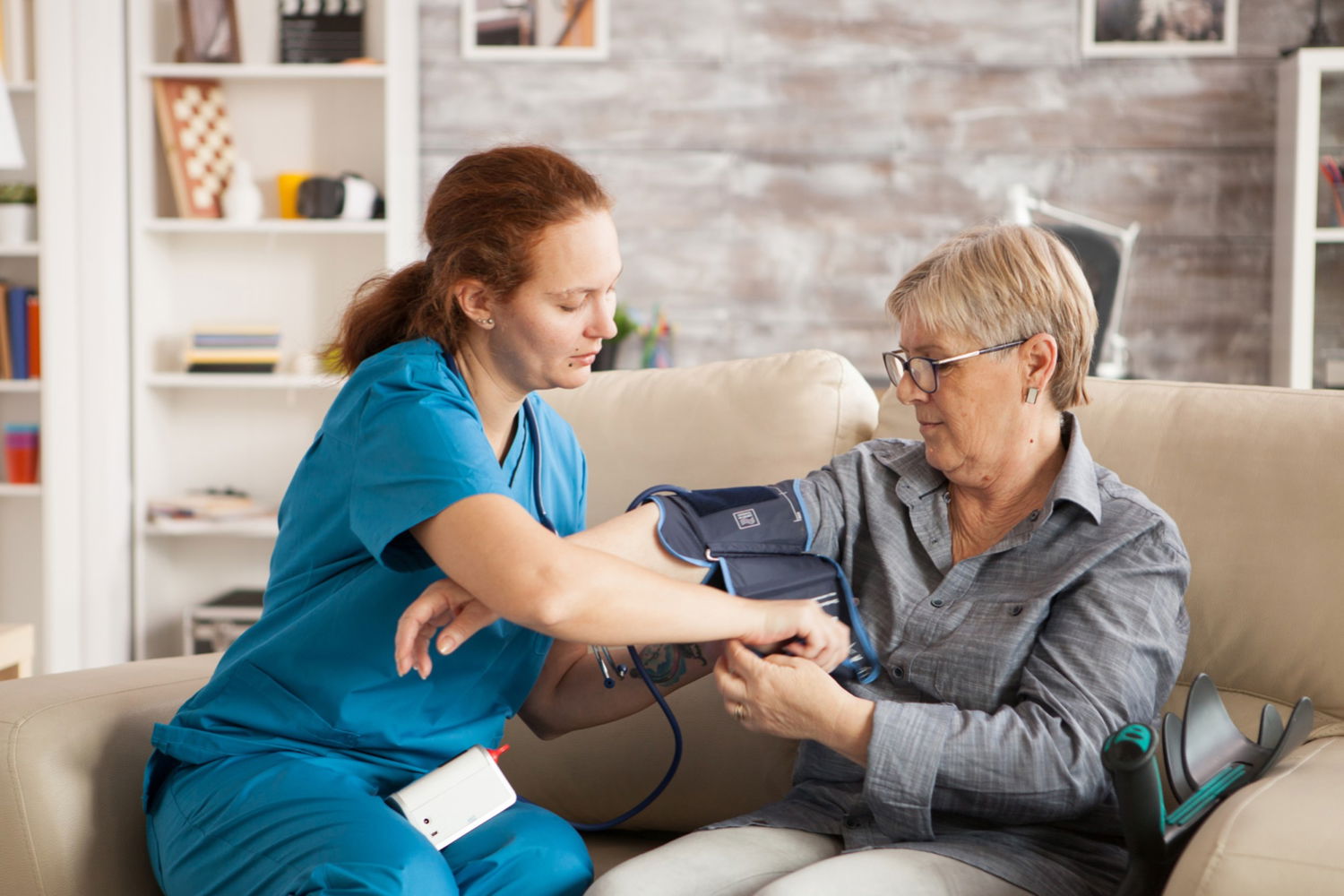 Female nurse using digital blood pressure device senior woman nursing home