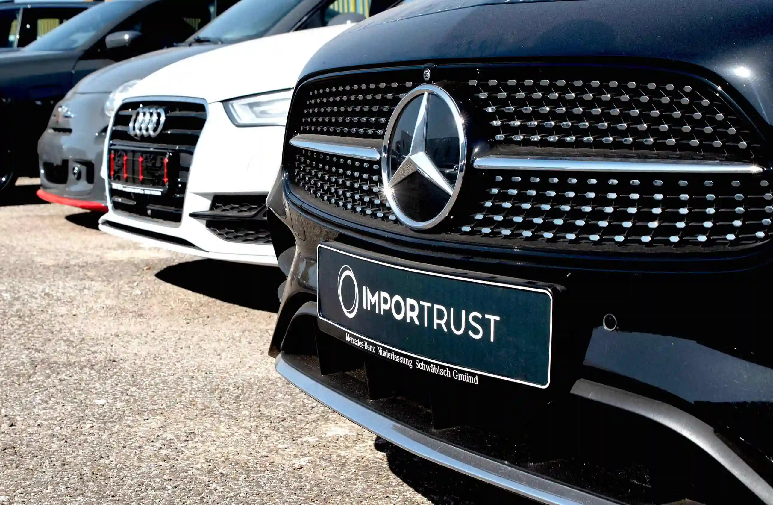 Fotografia de várias frentes de carros, incluindo um Audi branco e um Mercedes-Benz Classe C preto com a matrícula da Importrust