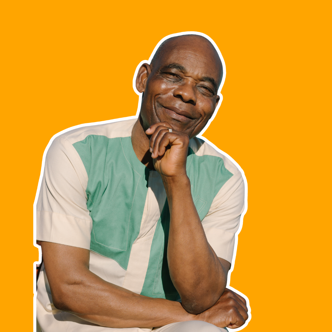 Man in casual clothes smiling thoughtfully with hand on chin, seated in front of a orange background.